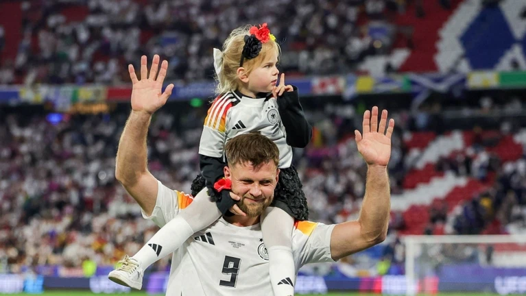 Deutschlands Spieler Niclas Füllkrug trägt nach dem Sieg seine Tochter Emilia durch das Stadion. — © Christian Charisius/dpa