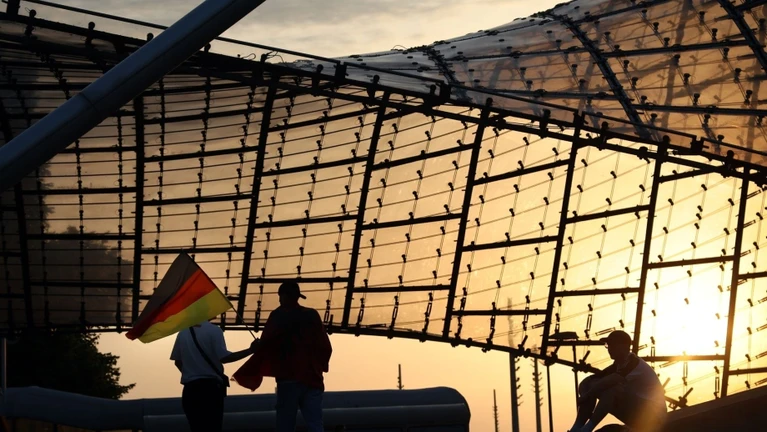 Fußball, UEFA Euro 2024, Deutschland – Ungarn, Vorrunde, Gruppe A, 2. Spieltag. Zuschauer mit Deutschlandfahne verlassen im Sonnenuntergang die Fanzone im Olympiapark nach dem Spiel. Die Fanzone im Münchner Olympiapark wird am Mittwoch nur eingeschränkt geöffnet sein. — © Karl-Josef Hildenbrand/dpa