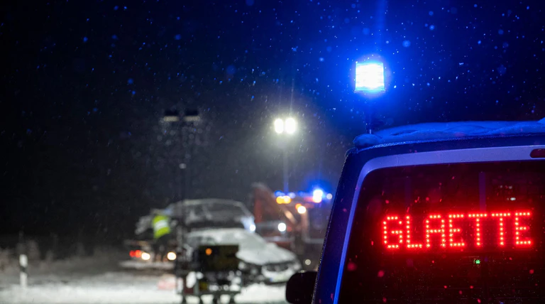 Auf der verschneiten Bundesstraße 12 warnt an einer Unfallstelle ein Polizeifahrzeug vor Glätte.  — © Stefan Puchner/dpa