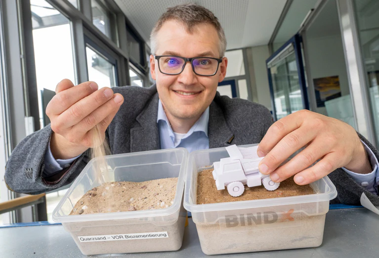 Luitpold Fried vom Start-Up-Unternehmen „Bind-X“ zeigt an einem Beispiel, wie mit einem speziellen Bindemittel aus ungefestigtem Sand, eine feste Verbindung entstehen kann, die zur Reduzierung von Staub auf unbefestigten Straßen führt.  — © Peter Kneffel/dpa