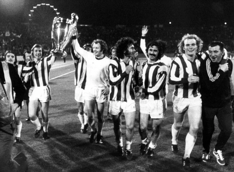 Die Bayern mit Paul Breitner (Mitte), Gerd Müller (3.v.r.) und Uli Hoeneß (2.v.r.) jubeln nach dem Gewinn des Europapokals der Landesmeister. (Archivfoto) — © picture-alliance / dpa