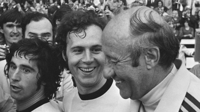  — © Von Bert Verhoeff für Anefo - Finale wereldkampioenschap voetbal 1974 in Munchen, West Duitsland tegen Nederland 2-1; v.l.n.r. Muller, Beckenbauer en trainer Schon na afloopDutch National Archives, The Hague, Fotocollectie Algemeen Nederlands Persbureau (ANeFo), 1945-1989,Auteursrechthebbende Nationaal Archief CC-BY-SA, Nummer toegang 2.24.01.05 Bestanddeelnummer 927-3108, CC BY-SA 3.0 nl, https://commons.wikimedia.org/w/index.php?curid=22812365