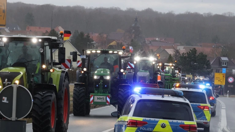 Polizeifahrzeuge begleiten Landwirte, die mit ihren Traktoren über eine Bundesstraße fahren. — © Bodo Schackow/dpa/Symbolbild
