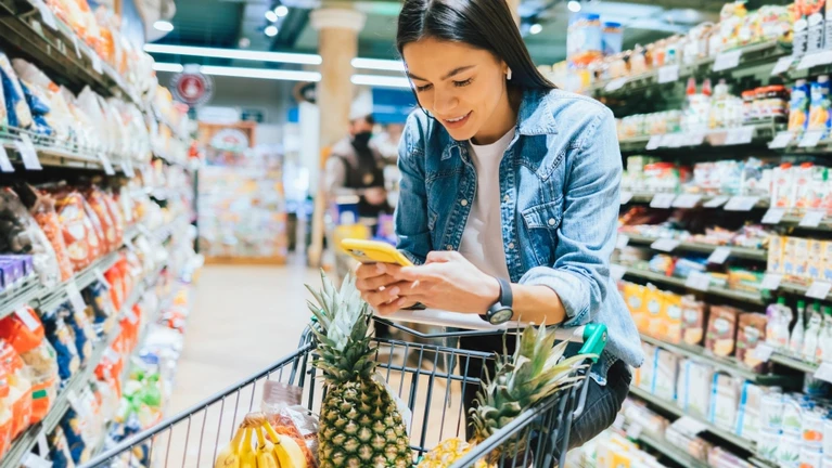 Frau shoppt mit Handy Einkaufswagen — © Bildnachweis: iprogressman / IStock