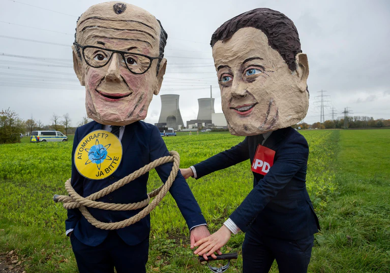 Als Bundeskanzler Friedrich Merz (l) und SPD-Vorsitzender Lars Klingbeil verkleidete Atomkraftbefürworter demonstrieren gegen die Sprengung. — © Stefan Puchner/dpa