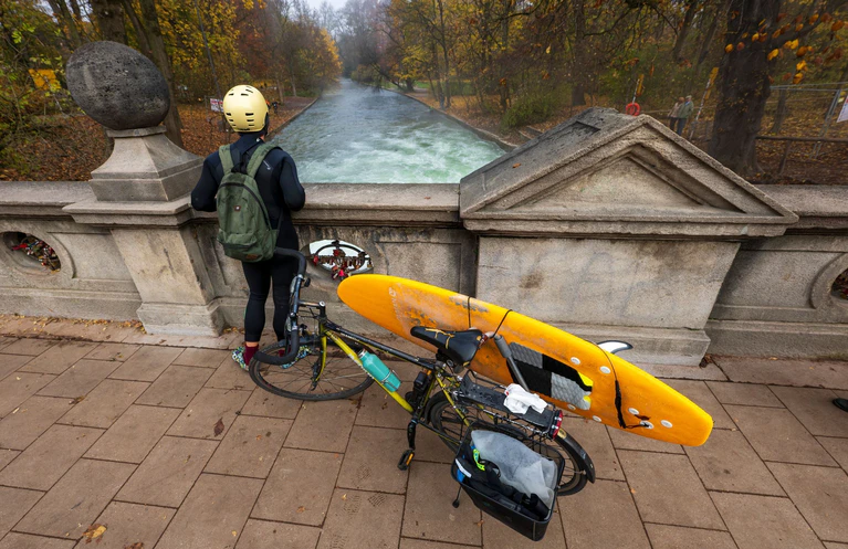 Ein Mann mit einem Surfboard an seinem Fahrrad schaut von einer Brücke auf die - nicht mehr vorhandene - Eisbachwelle im Englischen Garten. — © Peter Kneffel/dpa