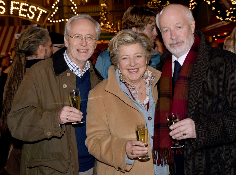 Die Schauspieler Joachim Hermann Luger (Hans Beimer, links) und die Schauspieler Marie-Luise Marjan (Mutter Beimer) und Bill Mockridge (Erich Schiller, rechts) posieren in der Außenkulisse mit Sektgläsern nach der Live-Ausstrahlung der 1559. Folge im Dezember 2015. — © picture alliance / dpa