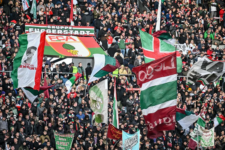Fans des FC Augsburg schwenken ihre Fahnen in der WWK-Arena. (Archivfoto) — © Harry Langer/dpa