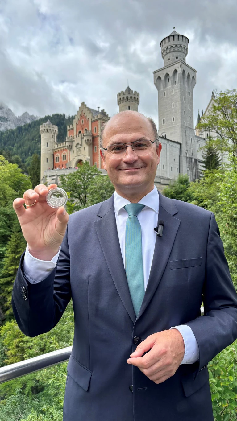 Finanzminister Albert Füracker (CSU)&nbsp;mit dem «Bayern Thaler» in der Hand vor Schloss Neuschwanstein. — © -/Bayerisches Finanzministerium/dpa
