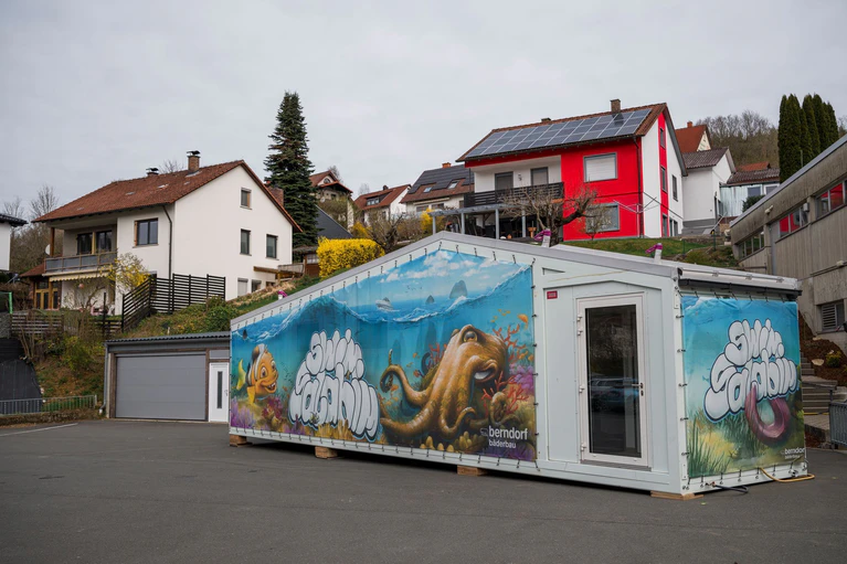 Bunt bemalt ist der Schwimmcontainer vor der Kasendorfer Schule.  — © Daniel Vogl/dpa
