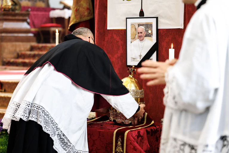 Pfarrer Daniel Lerch stellt die Tiara vor einem Bild des verstorbenen Papstes Franziskus ab.  — © Matthias Balk/dpa