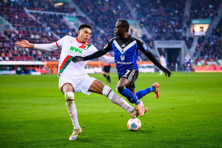 Augsburgs Noahkai Banks im Zweikampf mit Jean-Luc Dompé vom HSV. — © Tom Weller/dpa