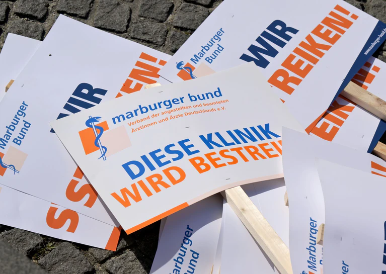 Plakate von Medizinern liegen auf dem Boden. Der Marburger Bund hat Ärztinnen und Ärztinnen in mehreren Bundesländern zum Streik aufgerufen. (Archivbild) — © Peter Kneffel/dpa