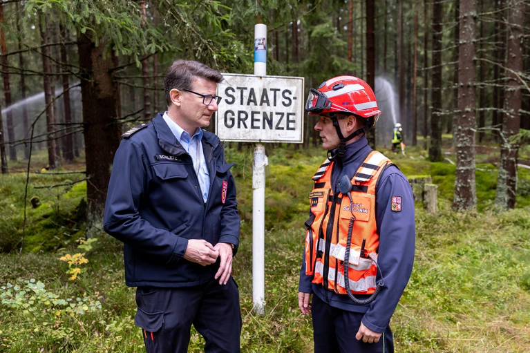 Wieland Schletz (l.), Kreisbrandrat des Landkreises Wundsiedel, und Martin Tomasek, Leiter des Feuerwehrdienstes der Region Karlsbad, sind bei der gemeinsamen Feuerwehrübung im Gespräch. — © Daniel Karmann/dpa