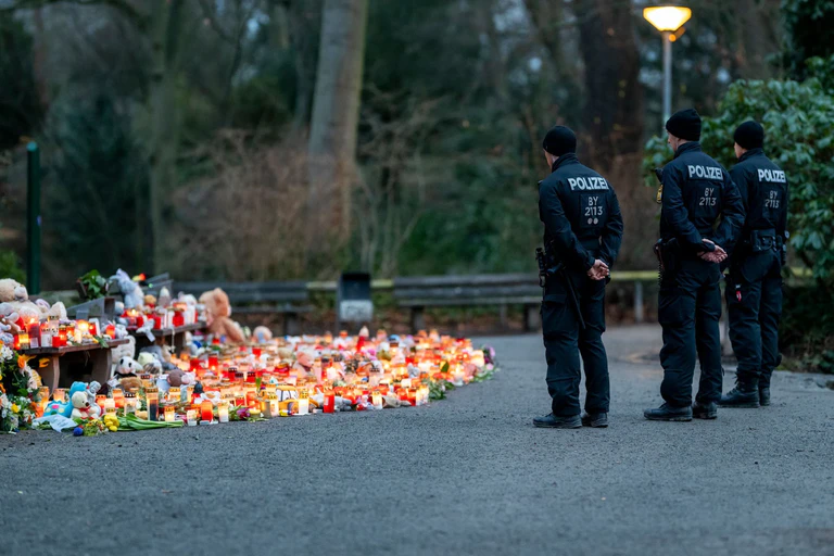 Mehrere Polizisten stehen vor der Ansammlung an Kerzen, Blumen und Kuscheltieren im Park. — © Jacob Schröter/dpa