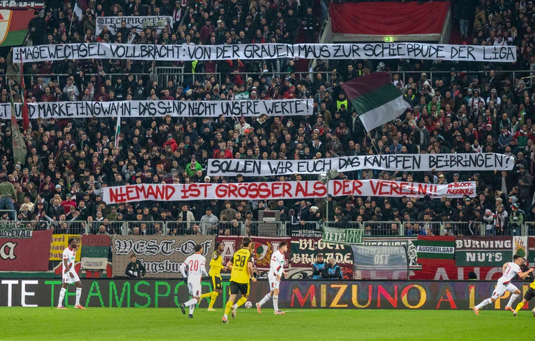 Die Augsburger Fans üben auf Spruchbändern Kritik am Weg der Vereinsführung mit Sandro Wagner. — © David Inderlied/Kirchner-Media/dpa