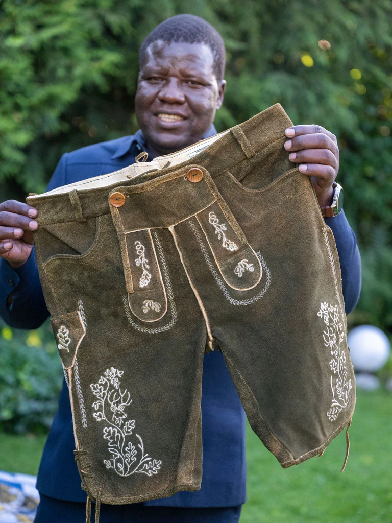 Alfred Okwonga, Bürgermeister der Stadt Gulu in Uganda, zeigt die ersten ugandisch-bayersichen Lederhosen.  — © Peter Kneffel/dpa