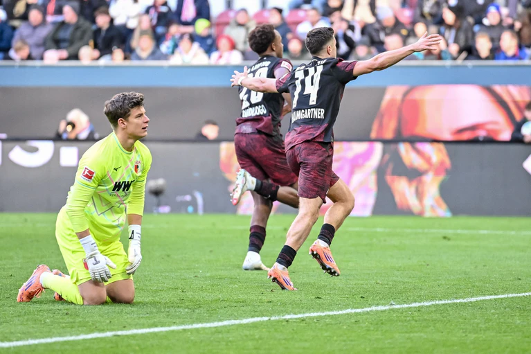 Augsburgs Torwart Finn Dahmen kauert bedröppelt am Boden, die Leipziger Assan Quedraogo (M) und Christoph Baumgartner (r) bejubeln das 0:5.  — © Harry Langer/dpa